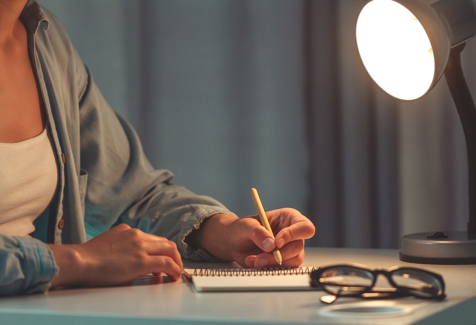 Person writing in a daily habit journal at a desk with morning light